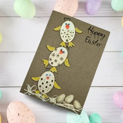 A handmade happy Easter chick card featuring three wooden chicks with orange wings, accompanied by pistachio shell eggs.