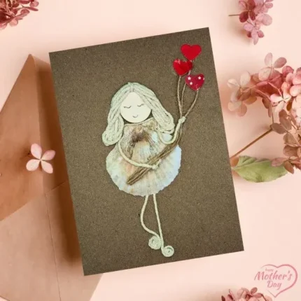 A Homemade Card for Your Mother featuring a girl holding a heart-shaped balloon, crafted with seashells on brown paper.