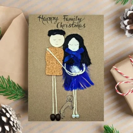 A personalised New Baby Christmas Card featuring a happy family, adorned with blue feathers, wood, cork, and coffee beans.