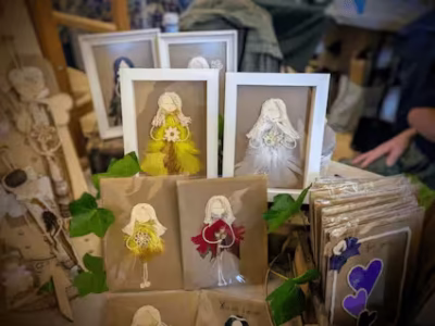 Heart in Creation’s Handmade Greeting Cards for Her feature whimsical fairy designs crafted from natural materials like feathers and flowers, displayed alongside green leaves and other handmade items.